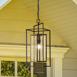 A contemporary, rectangular pendant from Urban Ambiance's Mainz Collection showcases seeded glass panels and hangs stylishly by a chain beneath a gabled porch roof, with measurements of 28-5/8''H x 14-1/8"W x 10''D in a Matte Black finish.