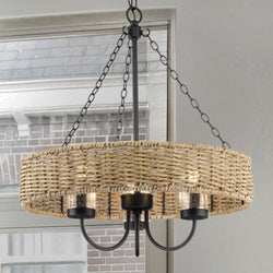 The UHP4781 Casual Indoor Chandelier from the Bexley Collection by Urban Ambiance, featuring weather-resistant rattan and a matte black metal frame with vintage-style bulbs, elegantly hangs in front of a window. Its dimensions are 21-1/2''H x 20"W x 20''D.